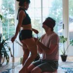 Blindfolded male client kneeling in front of Glory.