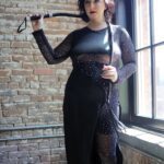 Tigress Lily wearing black and holding a flogger.