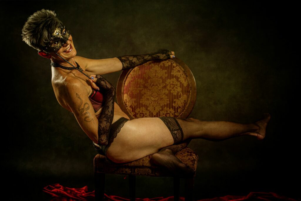 Liz Dake riding a chair while holding a mask in front of her face.