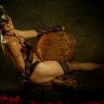Liz Dake riding a chair while holding a mask in front of her face.