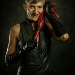 Liz with a cheeky smile holding a red flogger.