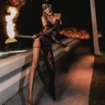 Ruby wearing a m ask and long black dress holding a burning stick performing outside.