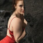 Jo standing by a rocky natural wall wearing a red velvety dress.