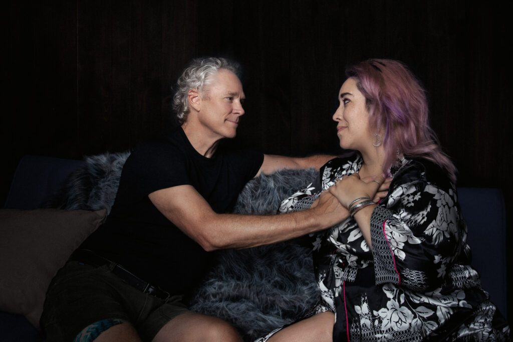 Female client sitting on the couch with Dan. His hand is on her chest.
