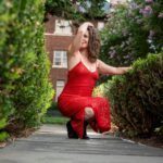 Aviva squatting on pavement in a red dress.