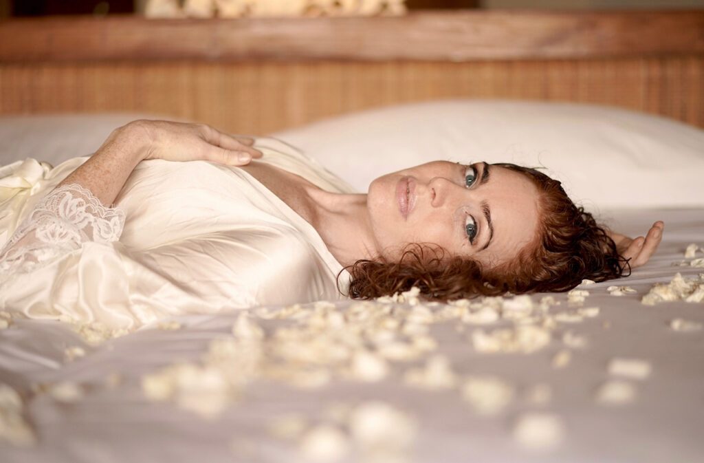 Jo on the bed in a white silky negligee.