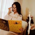 Natalia Knight wearing glasses and reading a book titled "Eros"