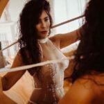 Natalia in a silky light white dress standing in front of the mirror.