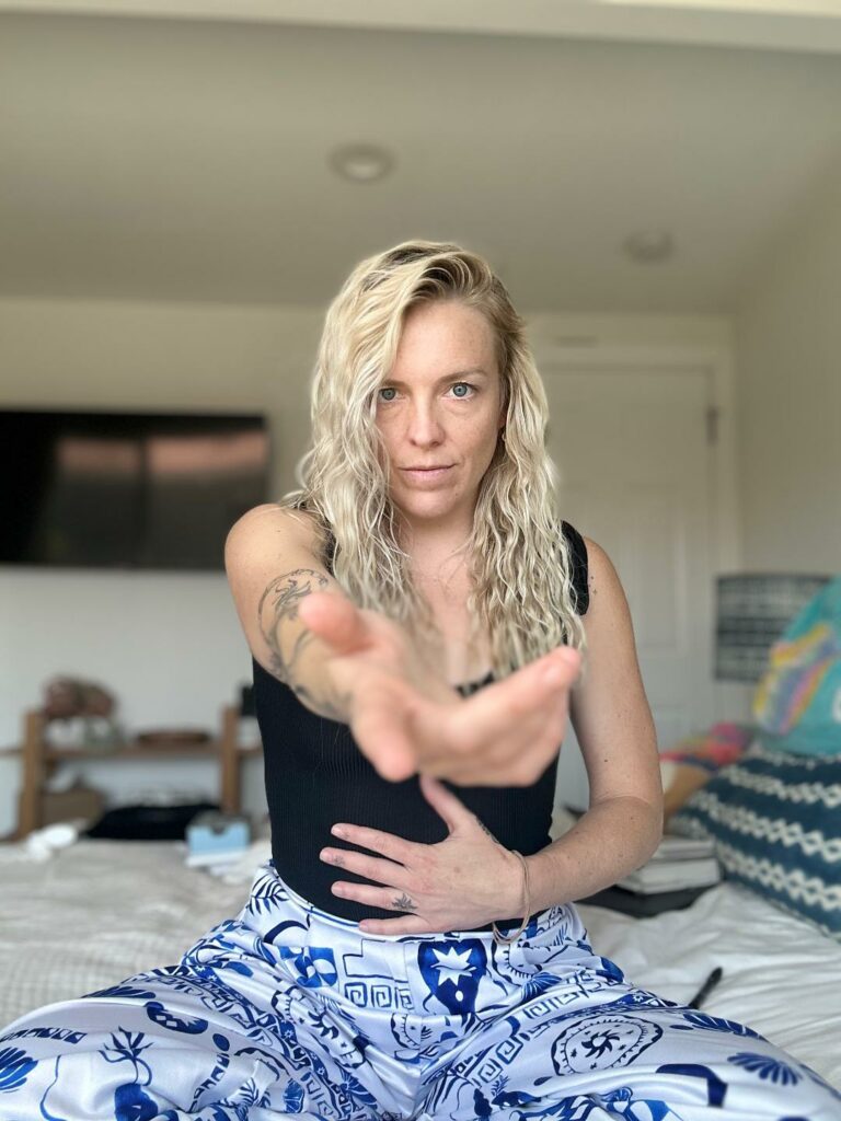Kat holding one hand on her belly and reaching out with the other.