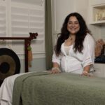 Lu standing by the massage table and smiling warmly.