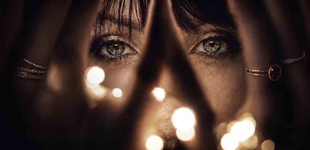 Artistic close-up of Lady Isabella looking to the camera through her fingers and some lights.