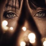 Artistic close-up of Lady Isabella looking to the camera through her fingers and some lights.