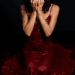 Lady Isabella in a red dress holding a white flower up by her face.