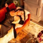 Sensual shot of Natalia lying down on the sofa in a black dress eyes closed.