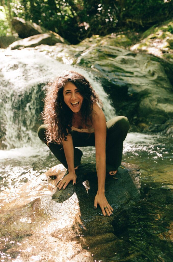 Wild smily on her face, Ariadne is squatting on a rock in a wild river.