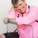 Kel sitting on a chair wearing a pink blouse.