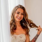 Helena by the window with a big smile in white dress.