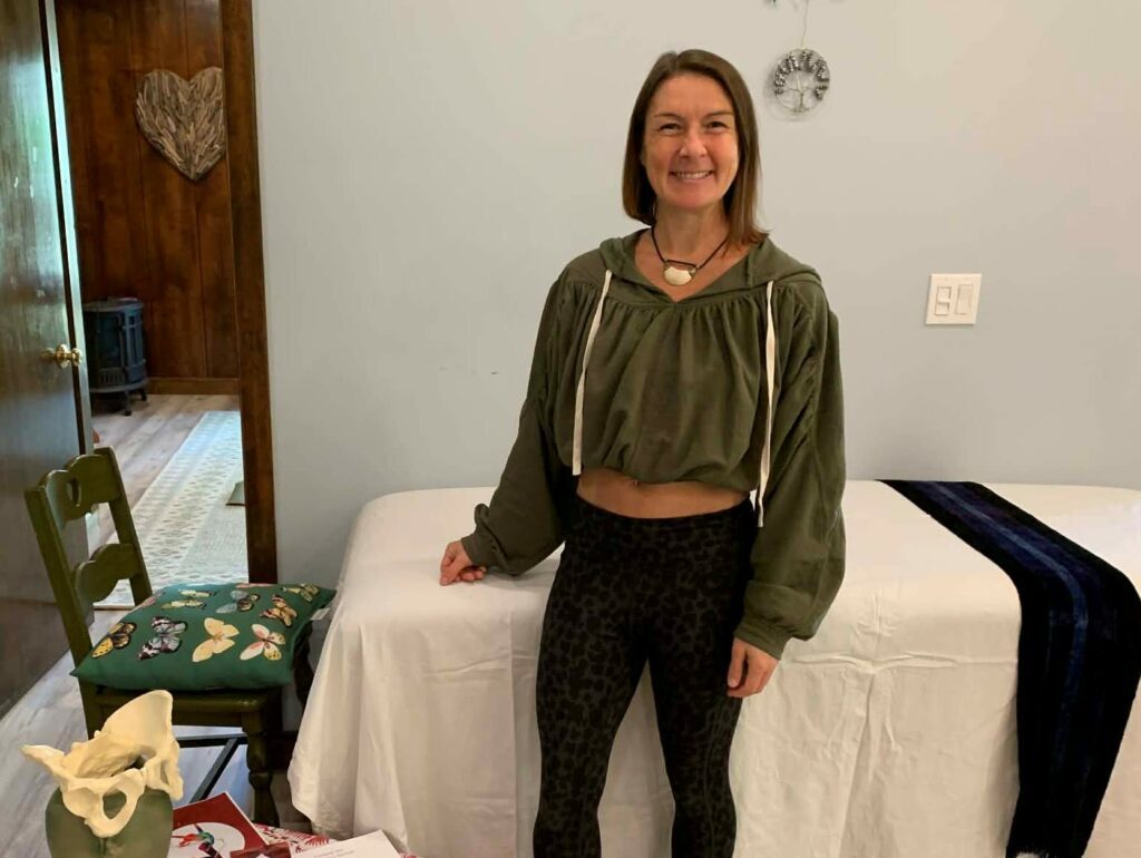 Wild Rose in her studio in front of a bed with a big smile.