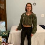 Wild Rose in her studio in front of a bed with a big smile.