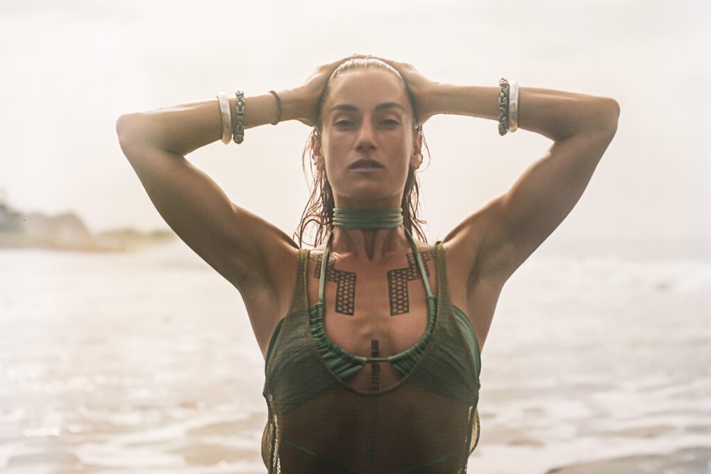 Paleta on the seashore hands connected behind her head.