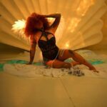 LadyKin in domina outfit, tattoos on legs exposed and hair covering the face.