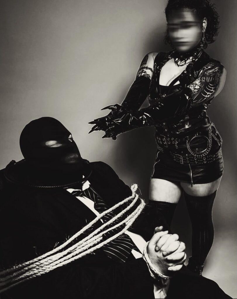 Male client is tied up while wearing a mask. LadyKin doing her work.