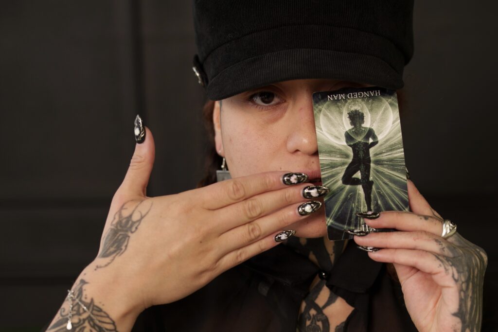 Holding a "hanged man" card to cover half of her face.
