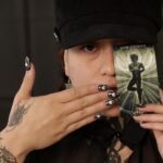 Holding a "hanged man" card to cover half of her face.