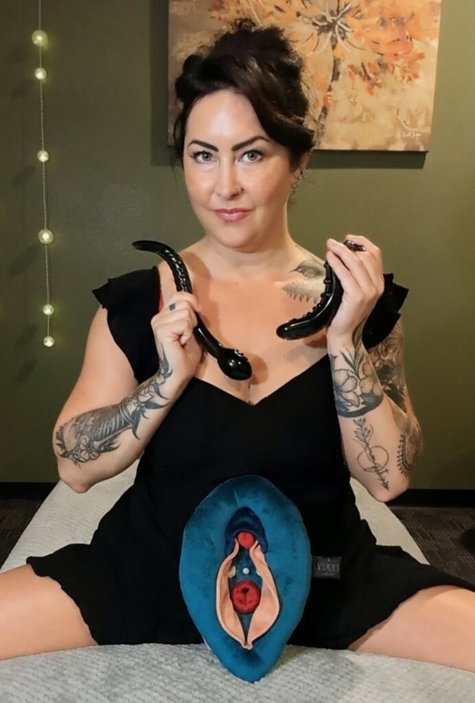Andrea holding some toys and showing her vulva-shaped cushion.