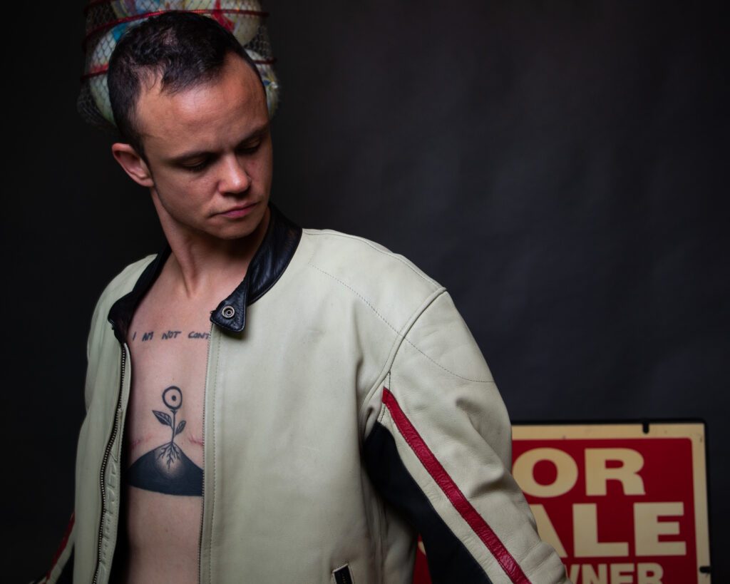 Wearing a gray shirt with his chest and tattoo exposed.