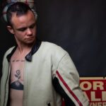 Wearing a gray shirt with his chest and tattoo exposed.