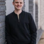 Grey leaning on a wall and smiling.