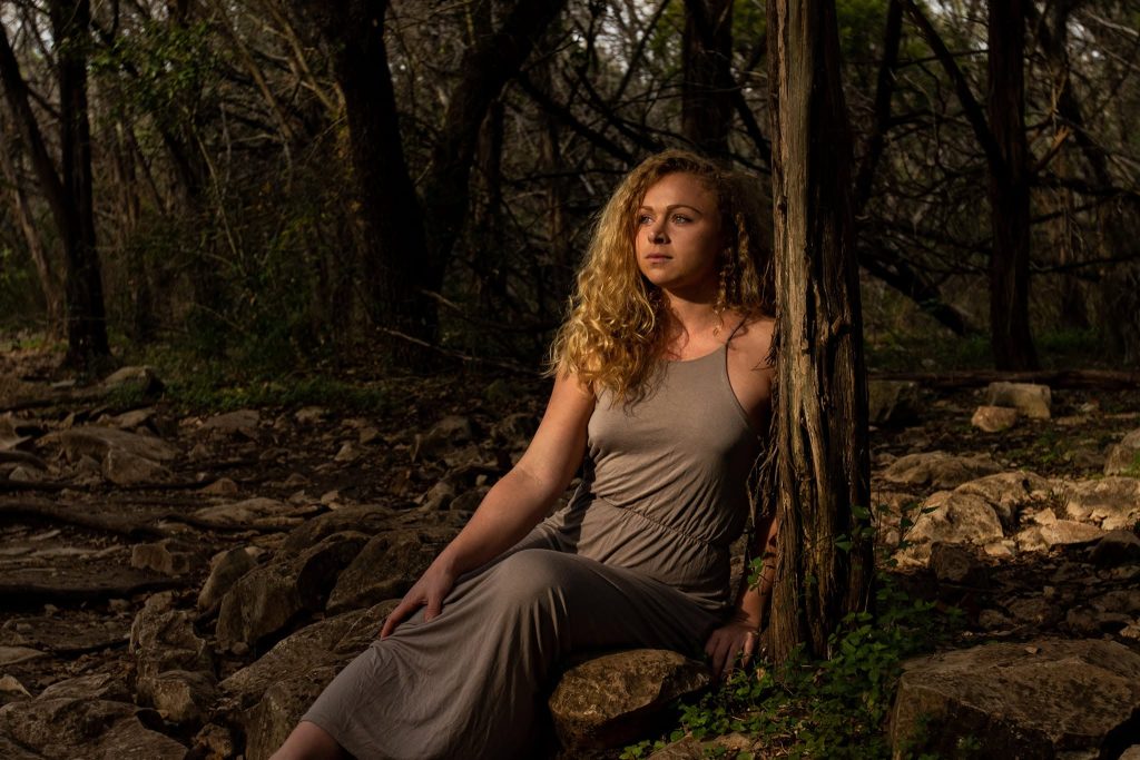 Gina Marie in a long grey dress leaning against a tree.