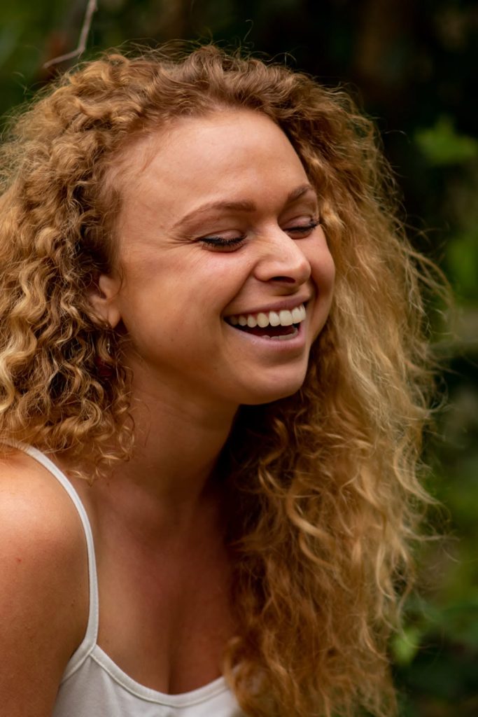 Close up of Gina - curly hair, big smile, eyes closed.