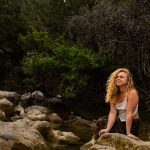 Gine Marie sitting on a rock by a stream.