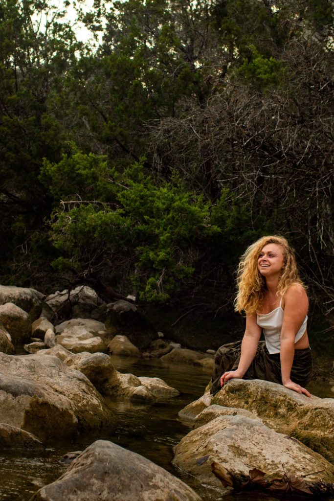 Gine Marie sitting on a rock by a stream.