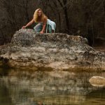 Gina climbing on a big rock by a river.