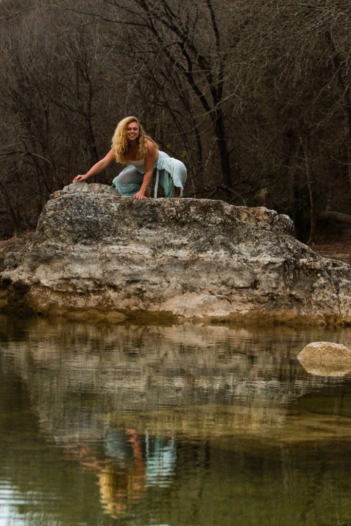 Gina climbing on a big rock by a river.