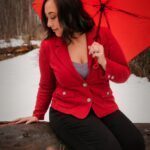 Outside in the nature. Miss Anna sitting on a log holding a red umbrella.