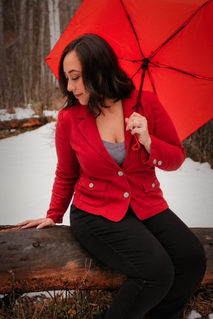 Outside in the nature. Miss Anna sitting on a log holding a red umbrella.